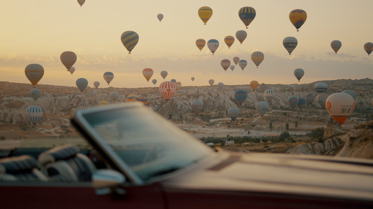 A breathtaking view of hot air balloons floating over Cappadocia's unique landscape at sunrise, captured from a car.